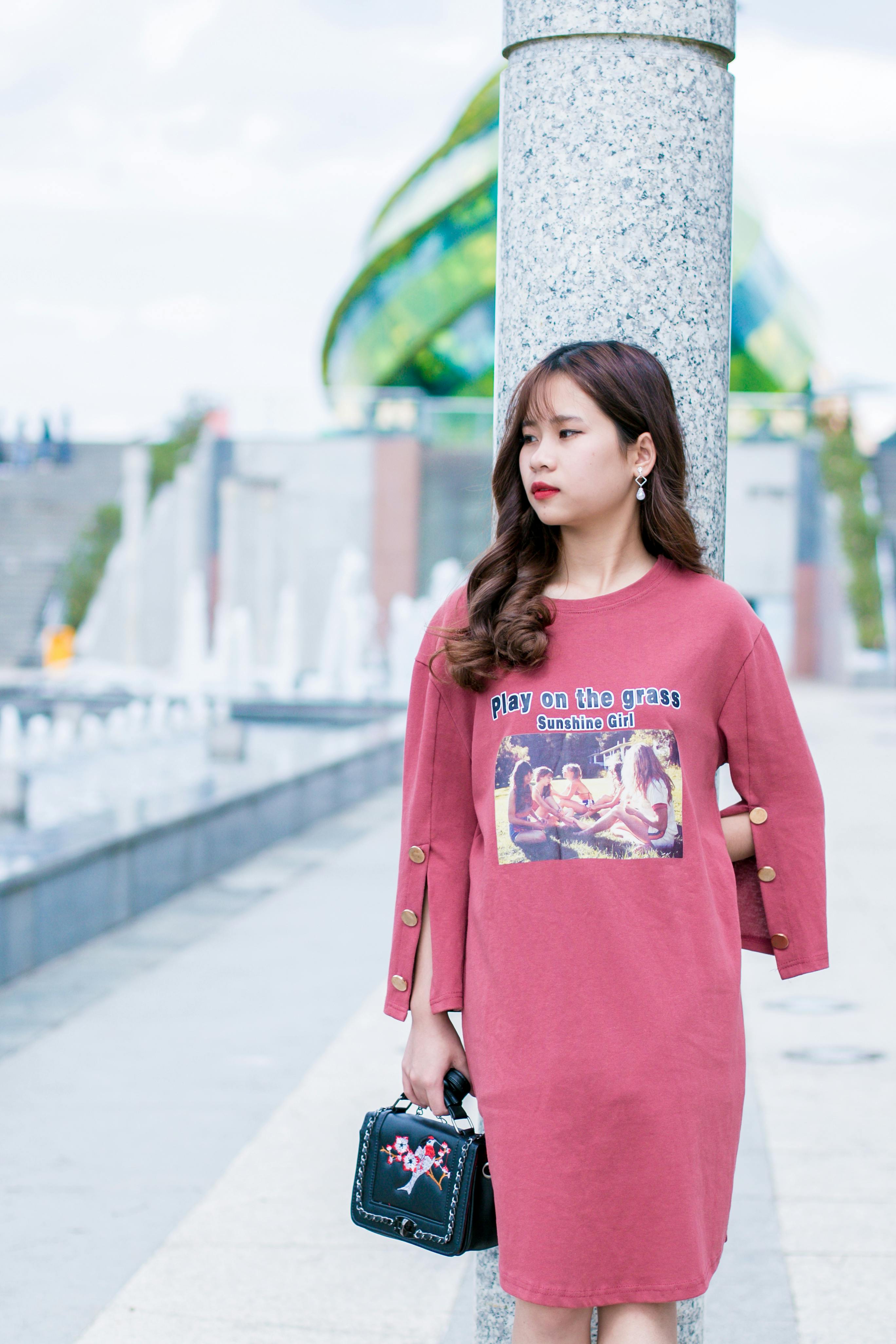 woman wearing pink crew neck long sleeved dress standing beside gray marble pedestal column