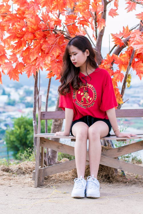 Free Woman Wearing Red Shirt Sitting on Bench Near Tree Stock Photo