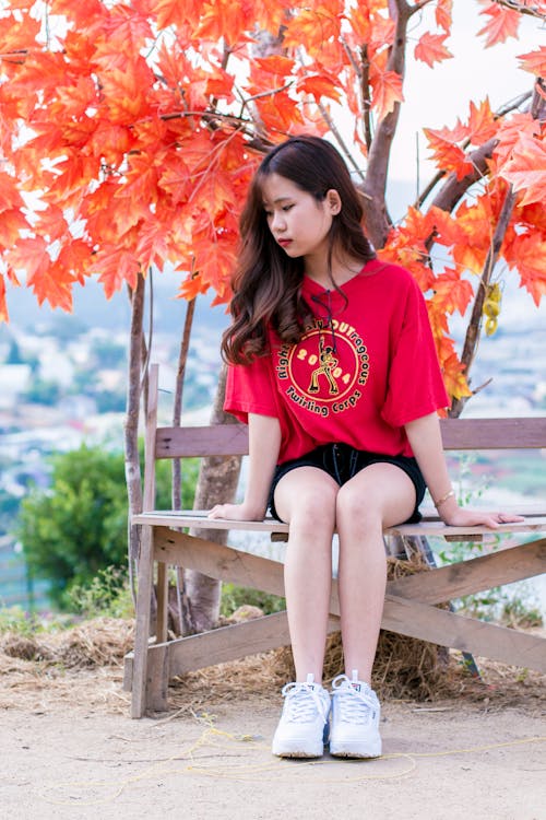 Woman Wearing Red Shirt Sitting on Bench Near Tree