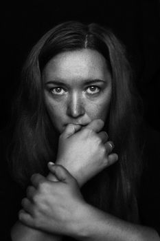 Dramatic black and white portrait of a woman with freckles in a thoughtful pose.