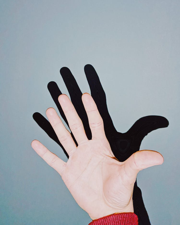 Illuminated Hand With Outstretched Fingers Casting Shadow On Wall