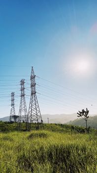 Electric pylons and power lines in a lush green field under a bright sunny sky.