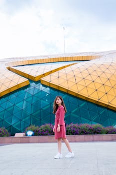 Stylish young woman poses in front of modern glass and steel architecture.