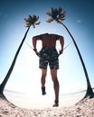 Silhouette of a man exercising on a sunny beach in Brazil, jumping rope between palm trees.