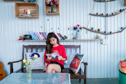 Woman in Red Shirt Reading Book While Sitting on Bench