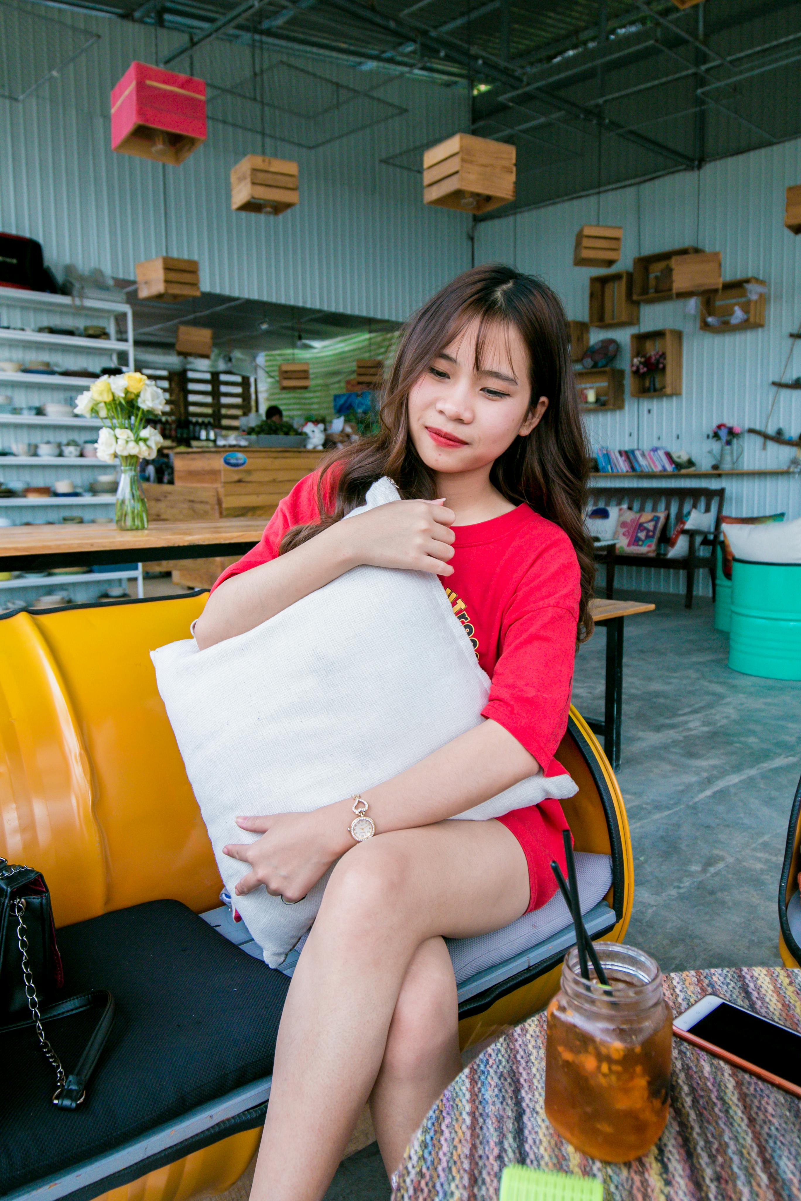 smiling woman wearing red lipstick and red shirt holding white throw pillow