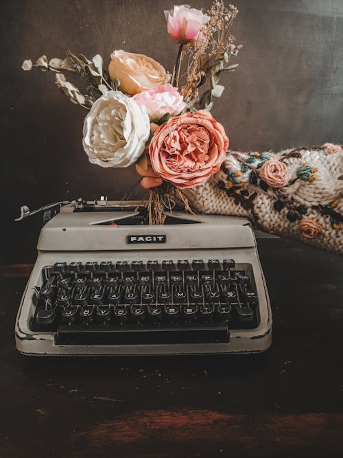A Hand Putting Stems of Flowers on Top of a Typewriter