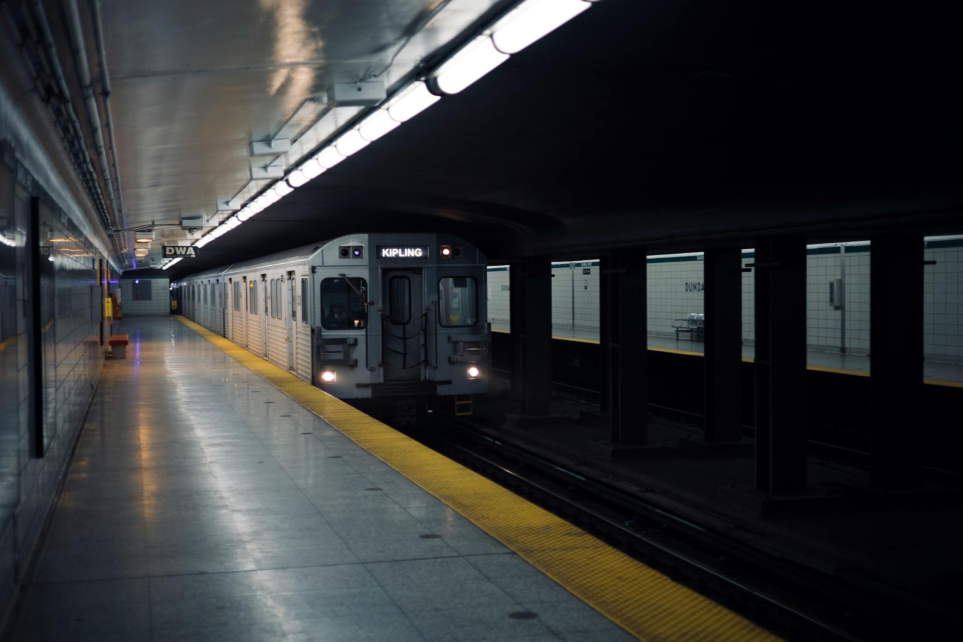 Toronto subway train approaching Dundas station platform in a dimly lit setting.