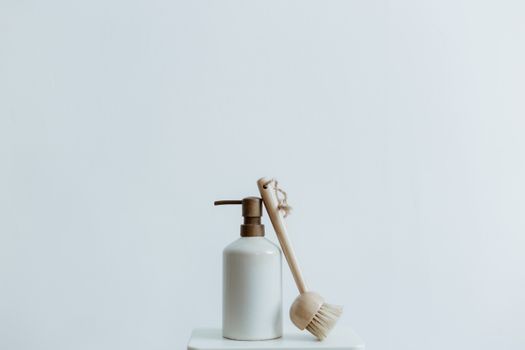 A minimalist soap dispenser and wooden brush set against a plain white background.