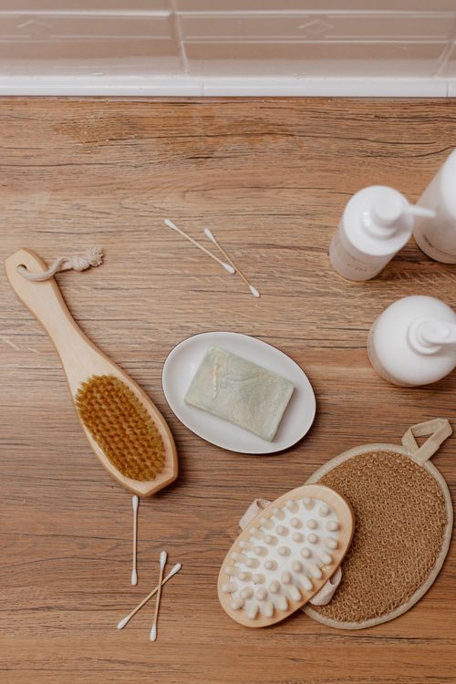Free Minimalist flat lay of bath essentials on wooden floor with brush, soap, and bottles. Stock Photo
