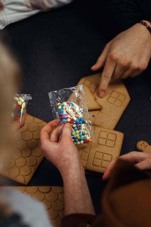 A Person Holding a Pack of Colorful Beads Over Gingerbread Houses