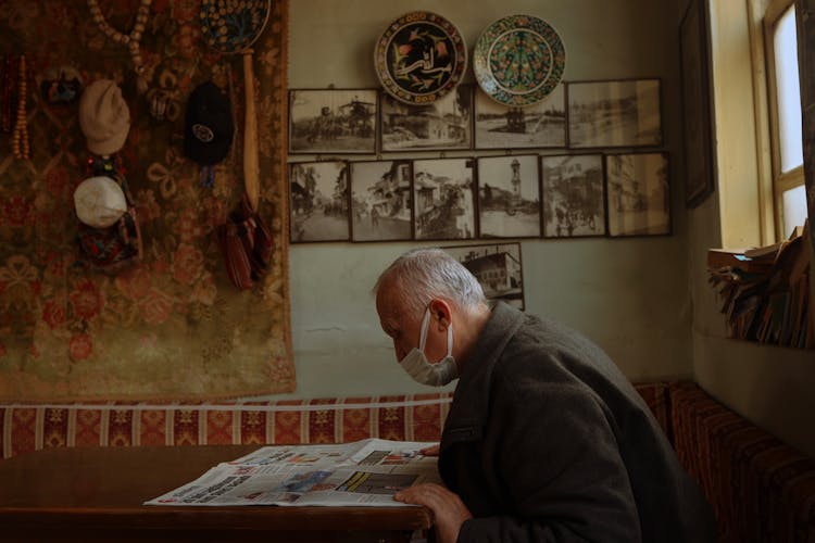 An Old Man In Face Mask Reading Newspaper 