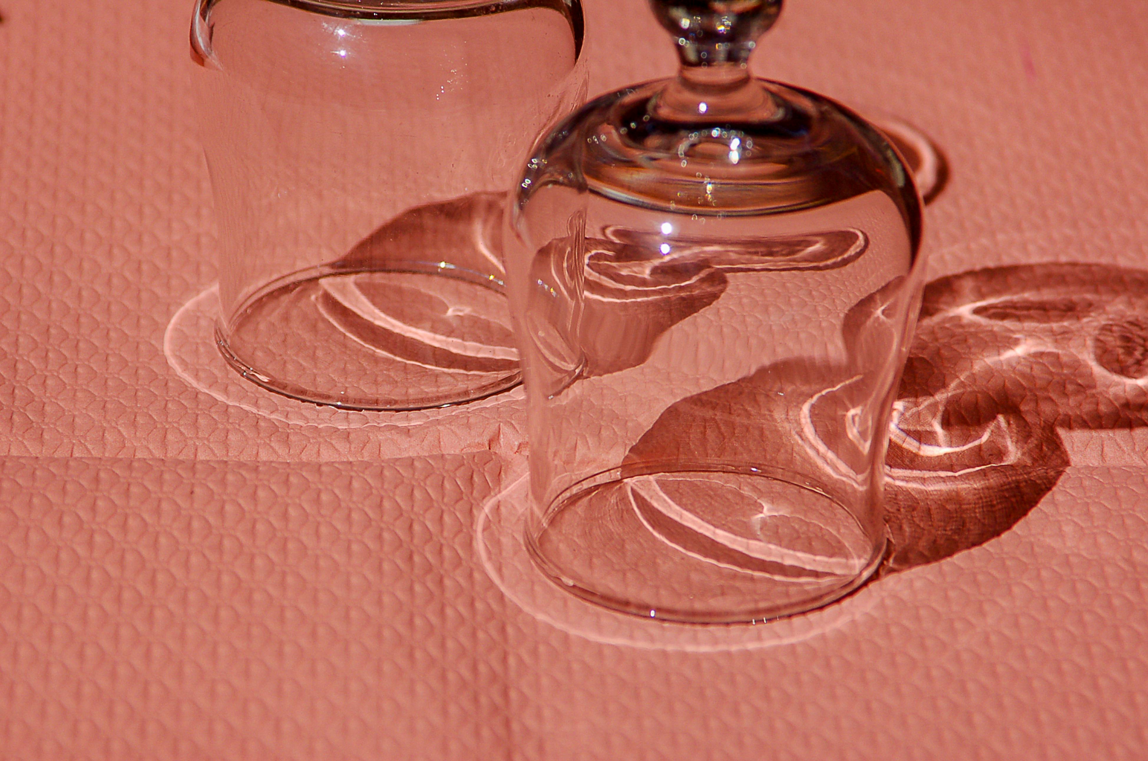 Close-up of inverted wine glasses casting intricate shadows on a pink textured surface.