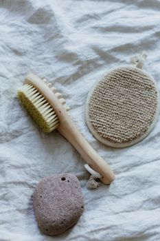 Flat lay of eco-friendly bath brush, pumice stone, and loofah on soft fabric.