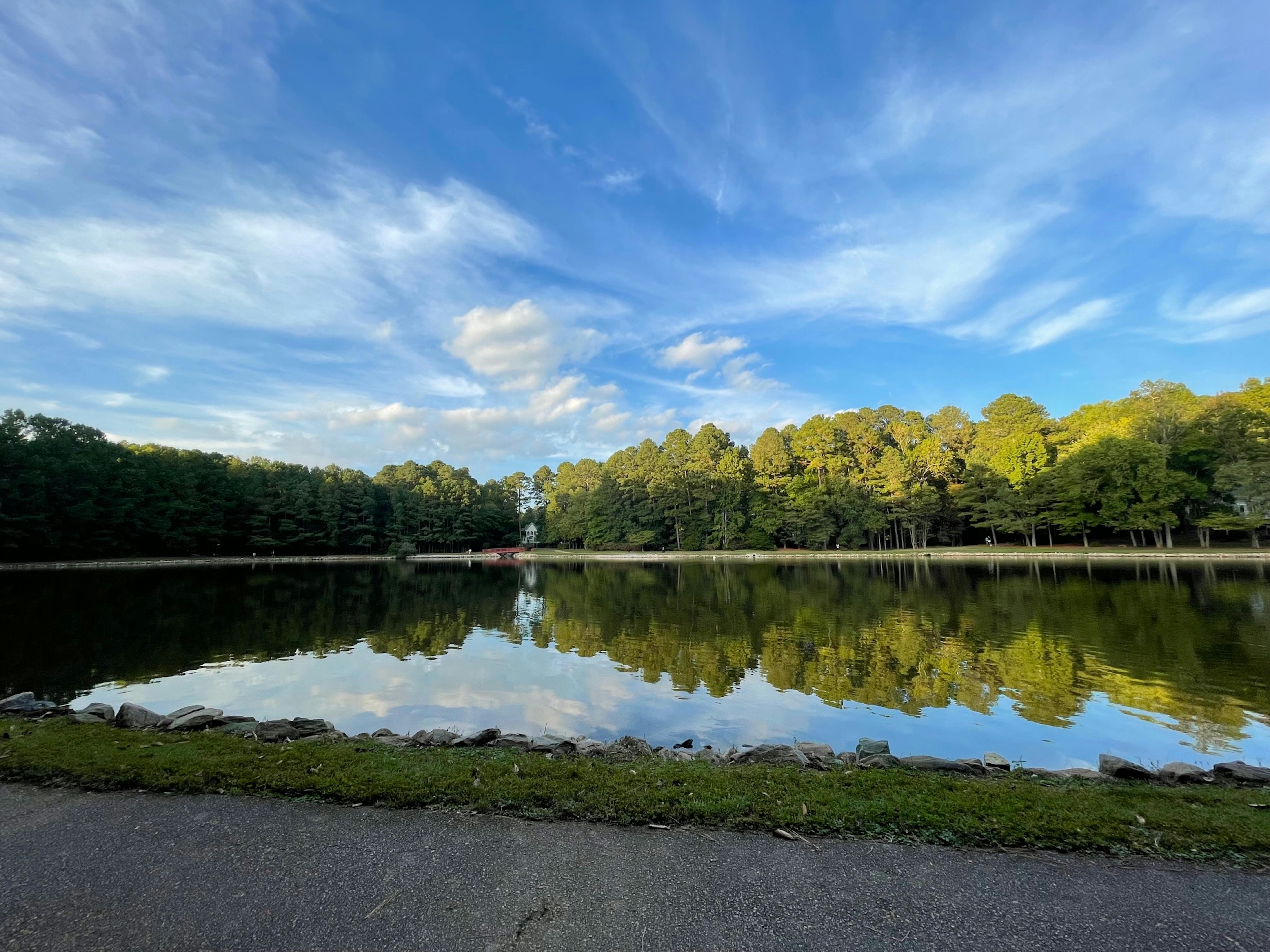 Scenic view of a peaceful lake with forest reflections and a vibrant sky in Cary, NC.