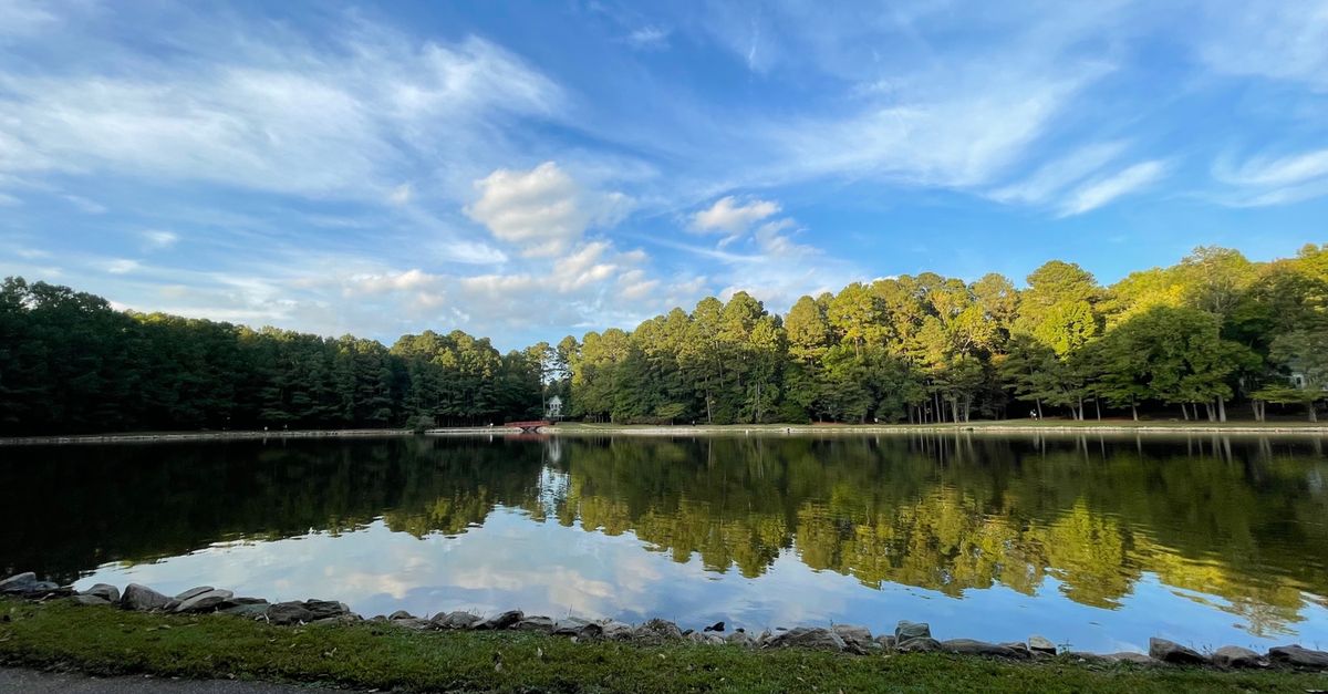 Scenic view of a peaceful lake with forest reflections and a vibrant sky in Cary, NC.