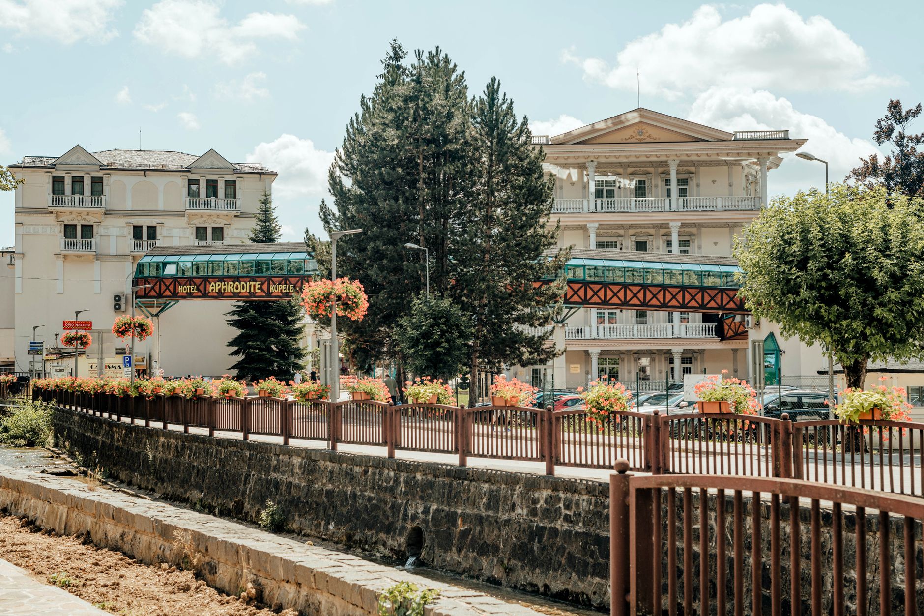 Exterior view of Hotel Aphrodite surrounded by lush greenery and floral displays under a bright blue sky.