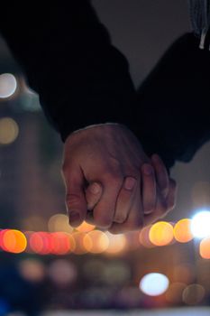 Close-up of a couple holding hands with a blurred city night background.