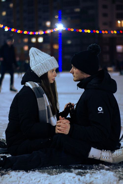 Free Couple enjoying a romantic moment on an ice rink surrounded by festive lights in winter. Stock Photo
