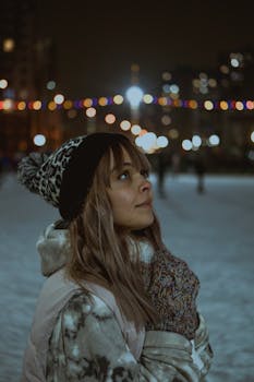 Young woman in warm winter clothing enjoying a snowy urban night with city lights.