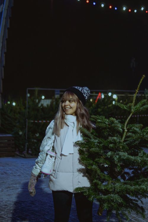 Free Smiling woman with beanie shopping for a Christmas tree outdoors at night. Stock Photo