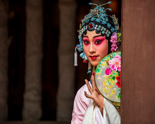 Free Portrait of a woman in vibrant traditional Chinese opera attire peeking around a corner. New Taipei City. Stock Photo
