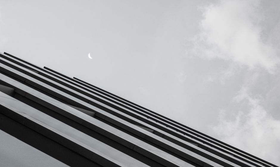 Una vista en ángulo bajo de un rascacielos moderno contra un cielo con una media luna visible en Santiago de Compostela, España.