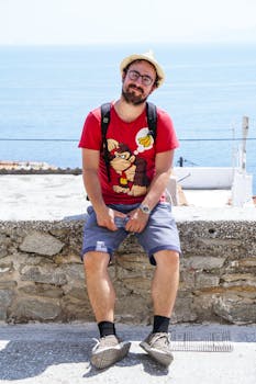 Casual tourist relaxing by the sea, wearing eyeglasses and a hat, enjoying a sunny day.