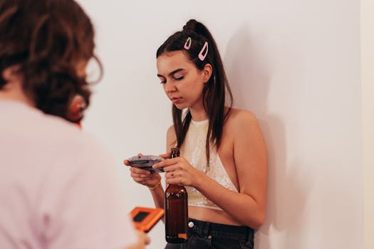 A young woman with hair clips plays a retro video game while holding a beer bottle indoors.