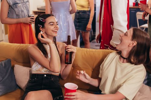 Free Two young women laughing and enjoying snacks at a lively indoor party. Stock Photo