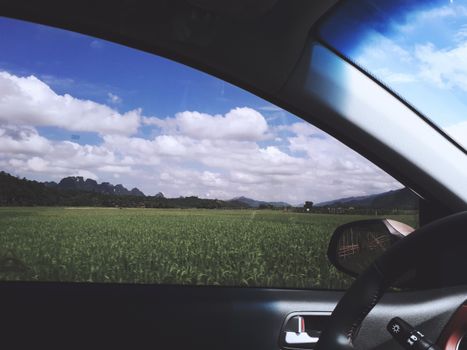 View from car window of vibrant green fields under a blue sky in Gia Lai, Vietnam.