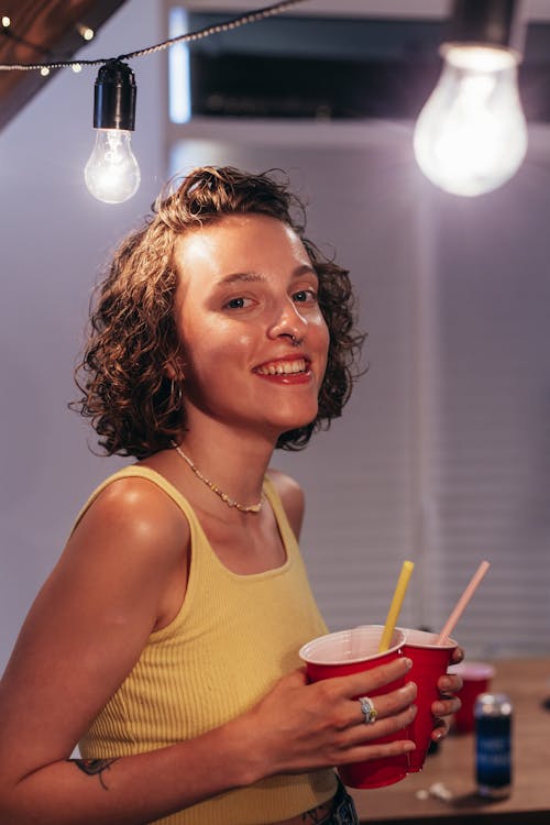 Close-Up Shot of a Woman in Yellow Sleeveless Shirt Holding Red Plastic Cups