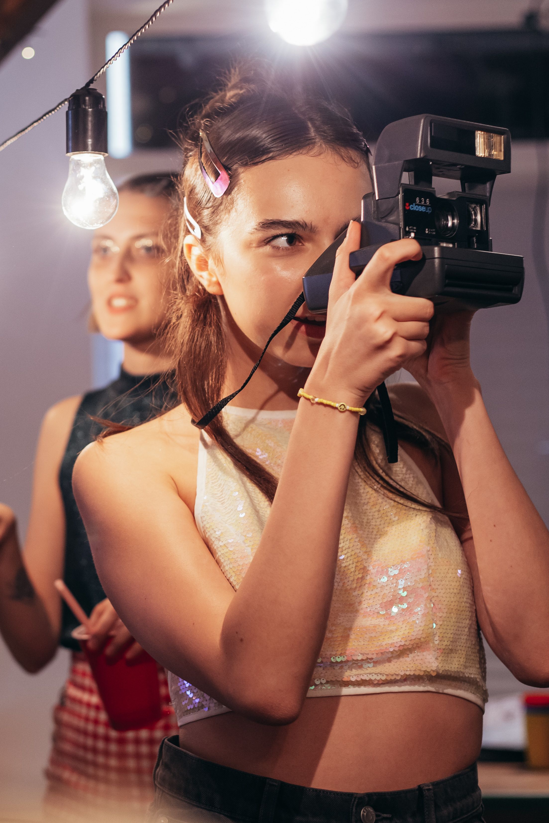 A young woman takes a picture with a vintage camera in a festive indoor setting.