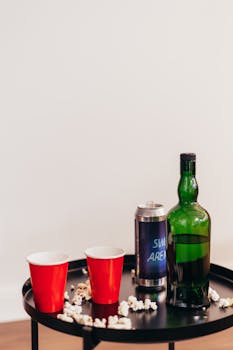 Still life of red cups and a liquor bottle on a black table with popcorn scattered around.