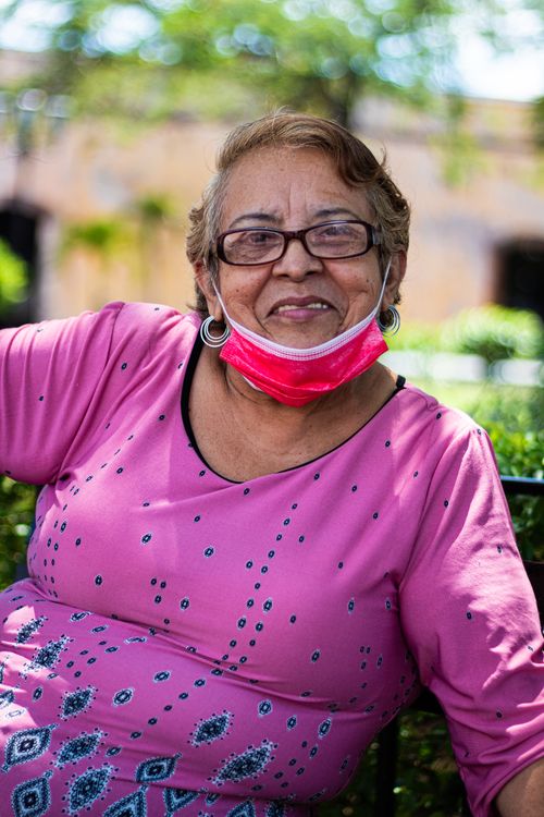 Free Elderly woman wearing a mask and eyeglasses, relaxing outdoors on a sunny day. Stock Photo