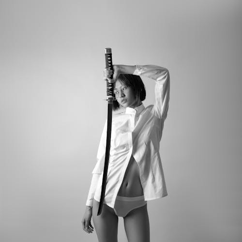 Free A Grayscale of a Woman Wearing a White Long Sleeves and an Underwear Holding a Katana Stock Photo