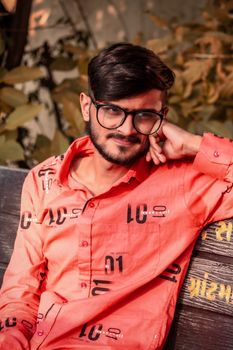Casual portrait of a young man in glasses and red shirt sitting on a bench outdoors.