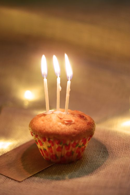 Free Warm birthday scene with muffin topped by lit candles on a cozy indoor setting. Stock Photo