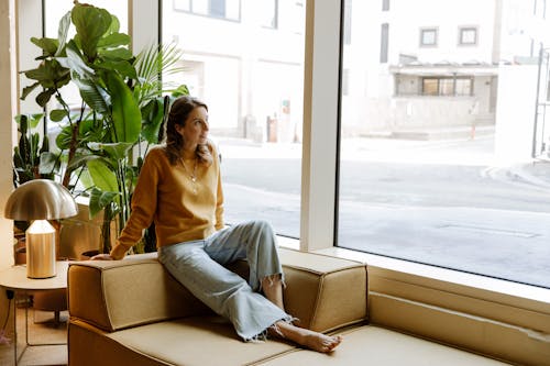 Free Young Woman Sitting on Sofa Looking Through Window  Stock Photo