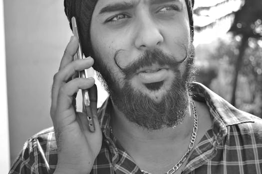 Black and white close-up of a bearded man using a smartphone outdoors.