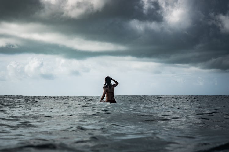 Woman In Sea Under Clouds