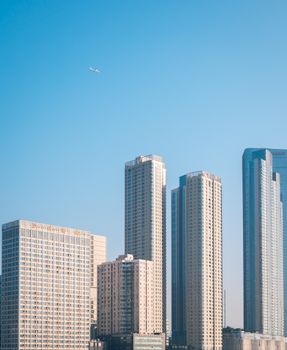 Tall modern skyscrapers under a clear blue sky with an airplane flying above.