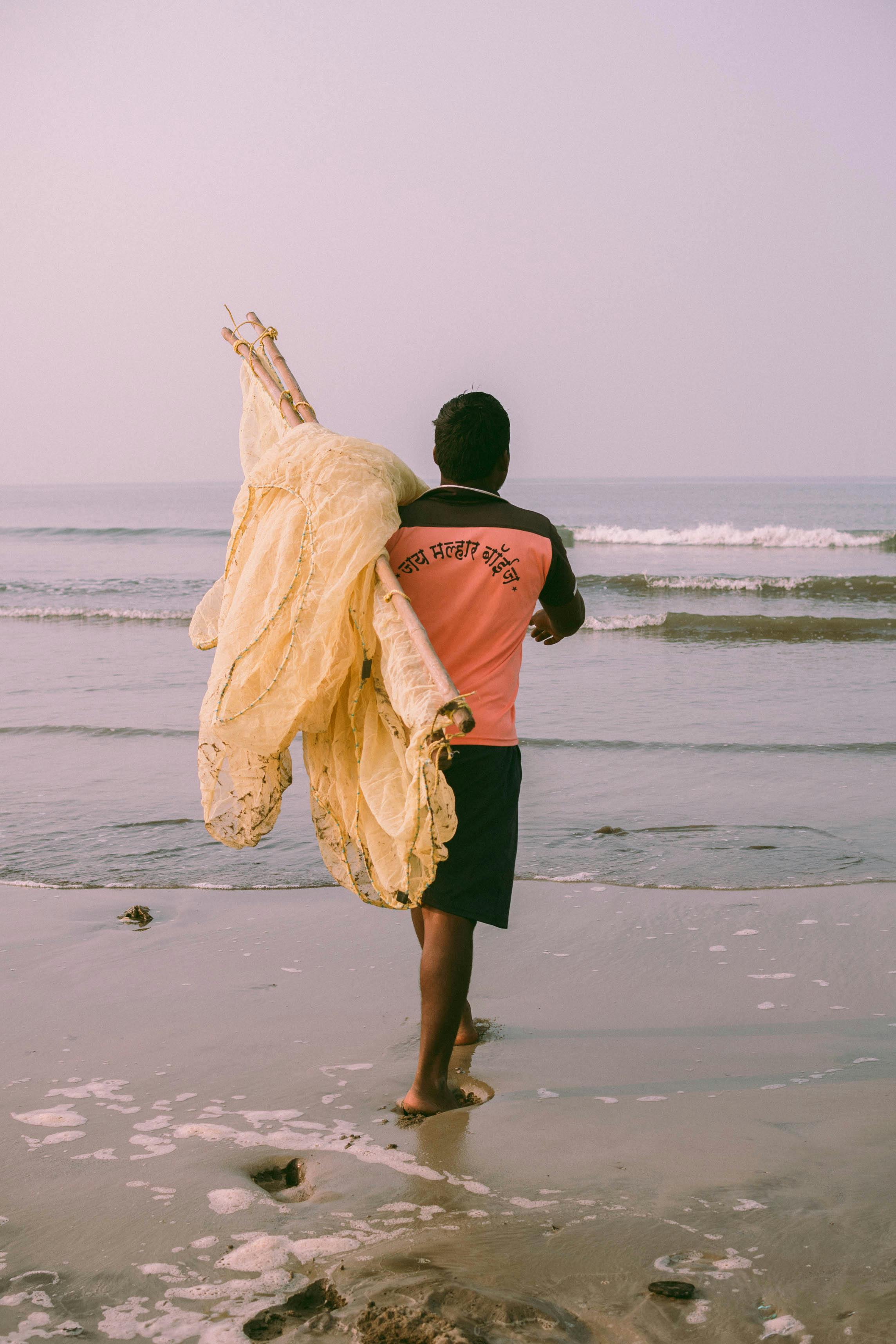 A fisherman carrying a fish net walks barefoot on Alibag beach, India.