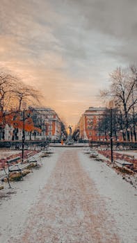 Serene winter scene of a snowy path flanked by benches in a Södermalm park at sunset.