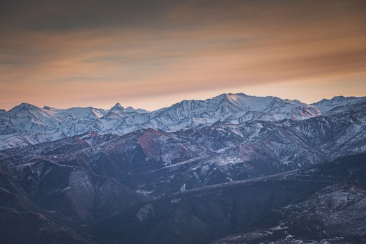 Experience the serene beauty of a snow-capped mountain range under a vibrant sunset sky.