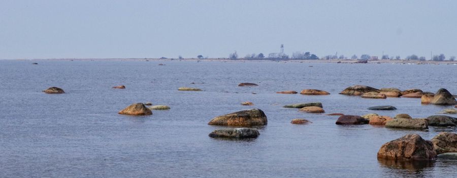Peaceful ocean view with rocks and distant lighthouse under a clear sky.