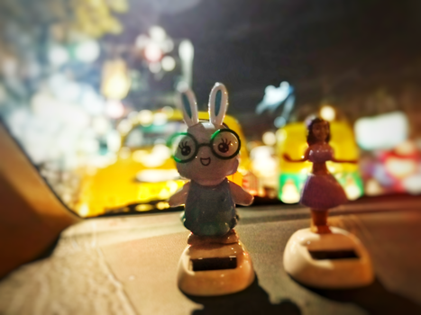 模糊的城市灯光背景下，汽车仪表板上古怪的兔子和娃娃雕像，营造出有趣的室内场景