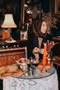 Hijabi Woman Sitting in Cluttered Room by Glass Table