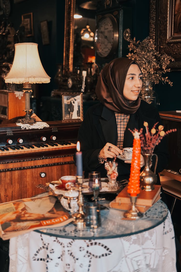 Hijabi Woman Sitting In Cluttered Room By Glass Table