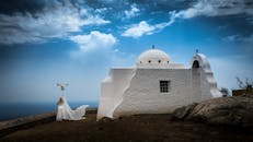 在悬崖边一座白色教堂旁，蓝天下，一个女人和一只鸽子构成了一幅宁静的场景